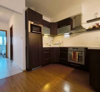 The kitchen of a two-room apartment with dark furniture and a wooden decor floor.