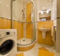 A bathroom with a washing machine, shower, and yellow tiles in a 2-room apartment.