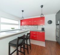 A kitchen in a family house with a red kitchen unit, a bar counter, and a floor with a wooden decor.