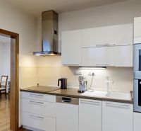 The kitchen of a 3-room apartment with white cabinets and a wooden floor decor.
