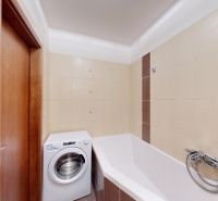 A bathroom with light tiles, a corner bathtub, and a washing machine in a 3-room apartment.
