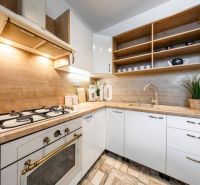 Kitchen in a 2-room apartment, light cabinets, open shelves, wooden decor flooring.