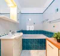 A bathroom with a bathtub and a sink in a 2-room apartment with blue and white tiles.