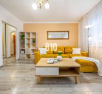 A living room in a two-room apartment with a yellow sofa and a floor with a wooden decor.