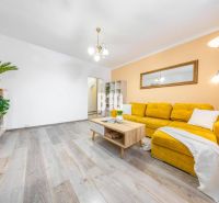 A living room in a two-room apartment with a wooden decor floor and a yellow sofa.