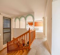 Interior of a family house with a wooden staircase and arched columns.
