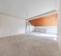 An unfurnished room with a radiator and a wooden ceiling in the attic of a family house.