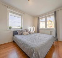 A bright bedroom with a bed, large windows, and a wooden decor floor in a two-room apartment.