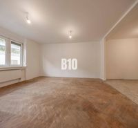 Living room in a three-room apartment with a wooden decor floor and large windows.
