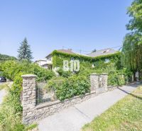 A family house in Bratislava - Old Town covered with greenery, surrounded by a stone fence and trees.