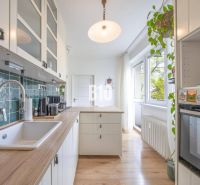 A kitchen in a 2-room apartment with a wooden decor floor and white cabinets.