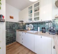 A kitchen in a 2-room apartment with a wooden decor floor and green tiles.