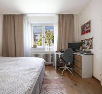 A bedroom in a two-room apartment with a desk and a wooden floor.