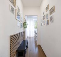 A hallway in a 2-room apartment with floor decor and hanging pictures on the walls.