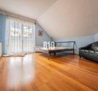 Bedroom in a family house with a bed, leather sofa, and wooden floor.
