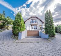 A family house in Marianka with shrubbery lining, a garage, and a partly cloudy sky.