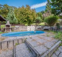 The garden of a family house in Marianka with a grill and a swimming pool surrounded by greenery.