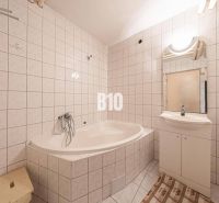 A bathroom with a bathtub and a sink in a family house, tiled with light tiles.