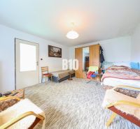 A room with a bed, cabinets, and an armchair in a family house. A carpet covers the floor.