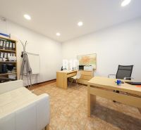 An office with wooden desks, a shelf with documents, a white chair, and a map on the wall.
