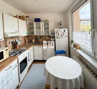 A kitchen in a 3-room apartment with a table, a refrigerator, and a kitchen unit with a sink.