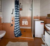 A bathroom in a 3-room apartment with orange tiles, a shower, a washing machine, and a toilet.