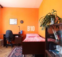 A room in a 3-room apartment with furnishings: bed, table, shelf, and exercise bike.