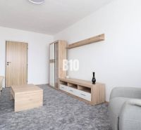Living room with a beige sofa, gray armchair, and furniture with a wooden decor in a 3-room apartment.