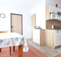 A kitchen in a 3-room apartment with a wood-patterned floor, a dining table, and cabinets.