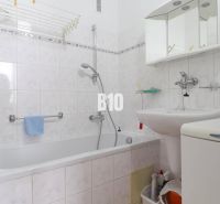 A bathroom in a 3-room apartment with a bathtub, sink, mirror, and washing machine.