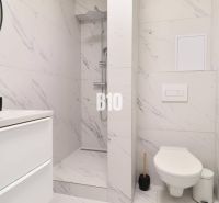 A bathroom with white tiles and a shower in a studio apartment.