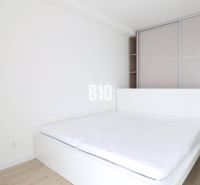 Bedroom in a studio apartment with a bed, built-in wardrobe, and wooden decor flooring.