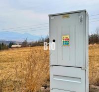 An electrical cabinet on a meadow, with hills and rural housing in the background.