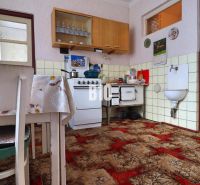 A kitchen in a family house with a tiled stove and a reddish-brown carpet.