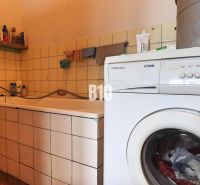 A bathroom in a family house with a bathtub, a washing machine, and cleaning products on a shelf.