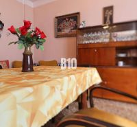 A dining room in a family house with flowers on the table, retro furniture, and glasses in the cabinet.