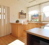 A kitchen in a family house with wooden decor, light furniture, and a window letting in daylight.