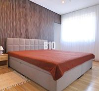 Bedroom with a bed, wallpapered wall, wooden floor decor, and furniture in a family house.