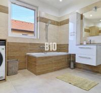 Bathroom in a family house with a bathtub, shower, and washing machine, floor with a wooden decor.