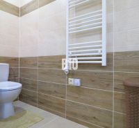 Bathroom with toilet, wood-patterned tiles, radiator, basket, wood-patterned floor.