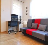 A room in a family house with a desk, chair, and colorful sofa, wooden decor flooring.
