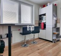 A kitchen with bar stools and a wooden decor floor in a 3-room apartment.