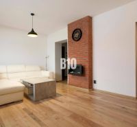 Living room in a 3-room apartment with a white sofa, brick wall, and wooden decor flooring.
