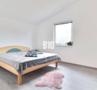 Bright bedroom in a family house with a bed, carpet, and wood-patterned flooring.