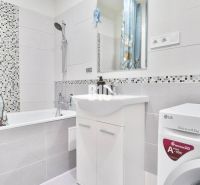 Bathroom in a 2-room apartment with a washing machine, a bathtub, and a floral-patterned curtain.