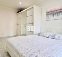 A bright bedroom with a double bed, a built-in wardrobe, and a wooden decor floor in a 2-room apartment.