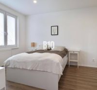 A bright bedroom with wood-decor flooring in a three-room apartment with a built-in wardrobe.