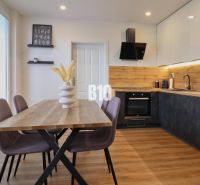 A kitchen in a 3-room apartment with a wooden decor, a table, and colorful chairs.