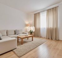 A living room of a family house with a beige sofa, a coffee table, and a wooden-patterned floor.
