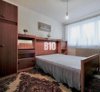 Bedroom in a 3-room apartment with carpet, wooden furniture, and a window with white curtains.